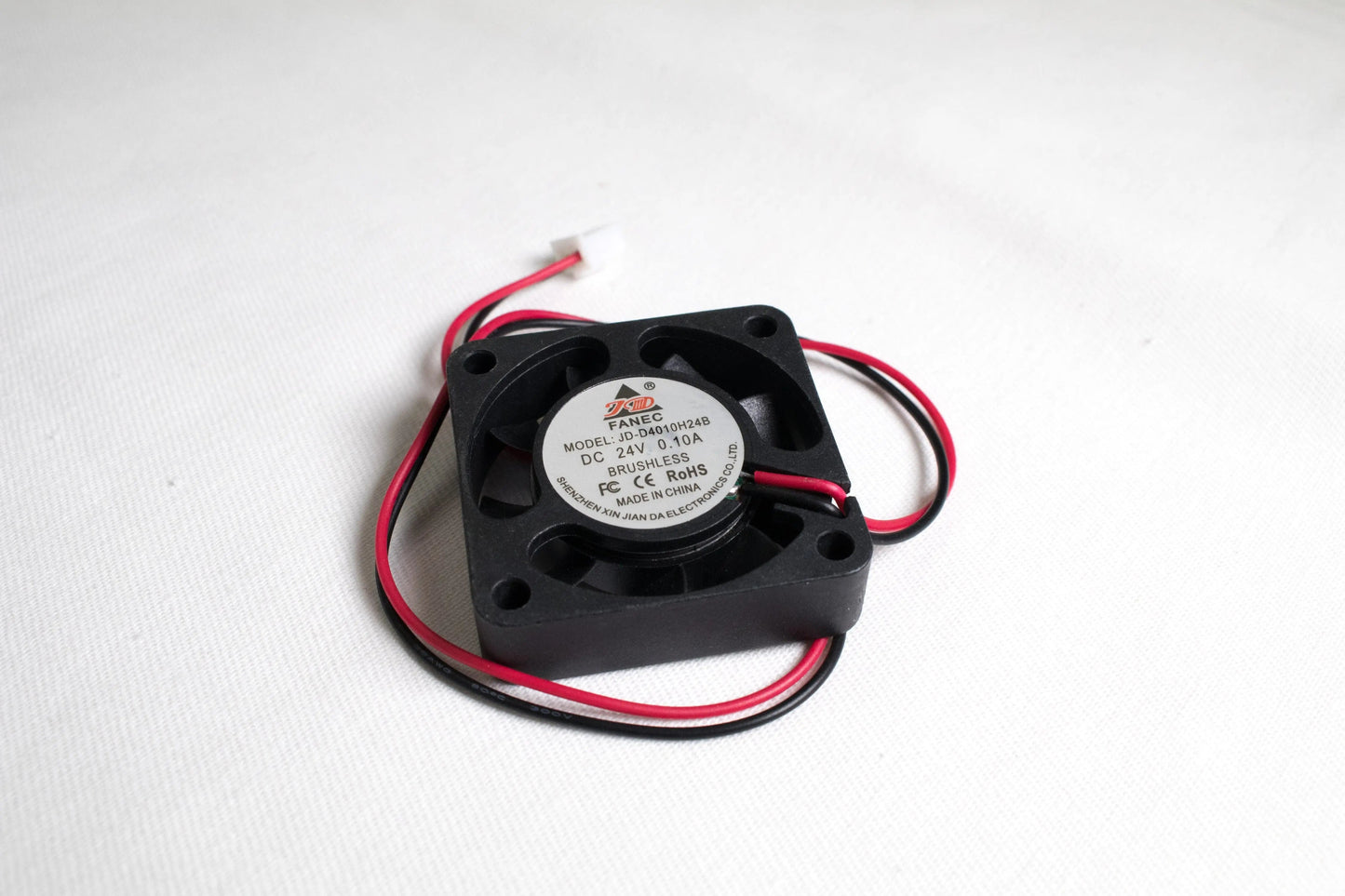 Petit ventilateur carré noir vu en trois quarts, avec câbles rouge et noir en boucle sur fond blanc