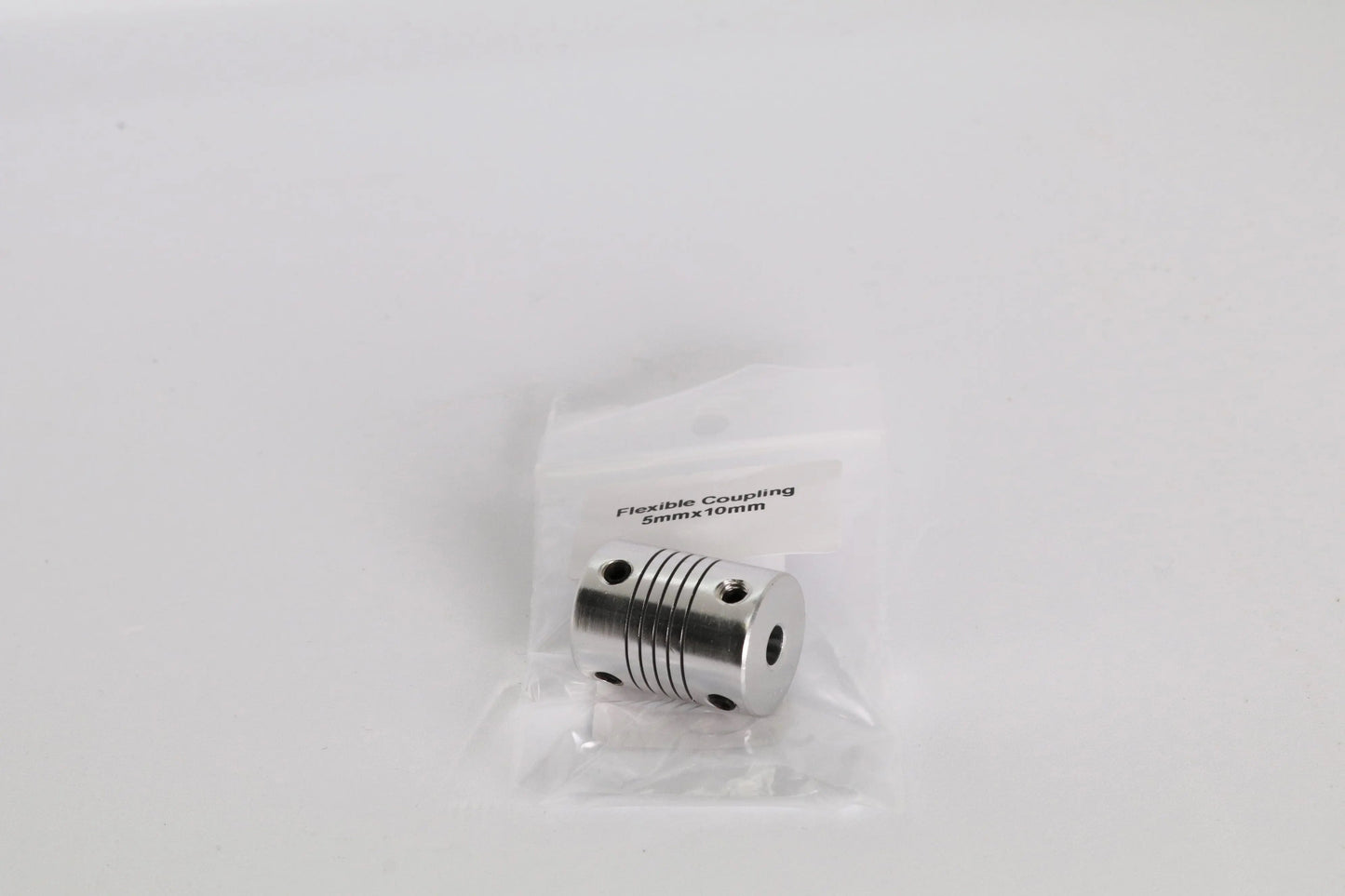 Un accouplement flexible métallique dans un sachet plastique transparent, posé sur fond blanc