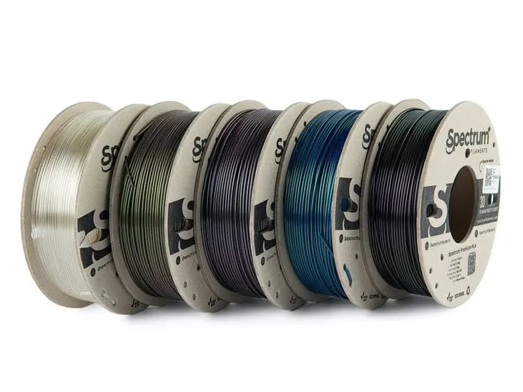 Cinq bobines de filament alignées de côté, aux teintes blanc, vert, gris, bleu et noir