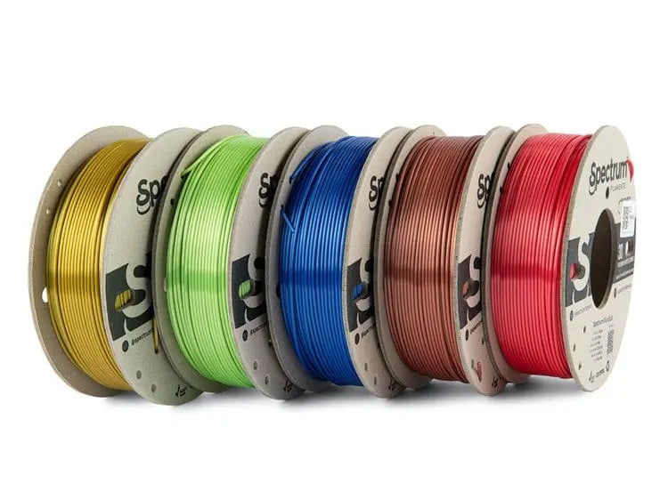 Cinq bobines de filament en couleurs or, vert, bleu, cuivre et rouge, alignées sur fond blanc