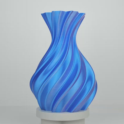 Vase imprimé en bleu, à facettes torsadées, posé sur un socle blanc sur fond gris