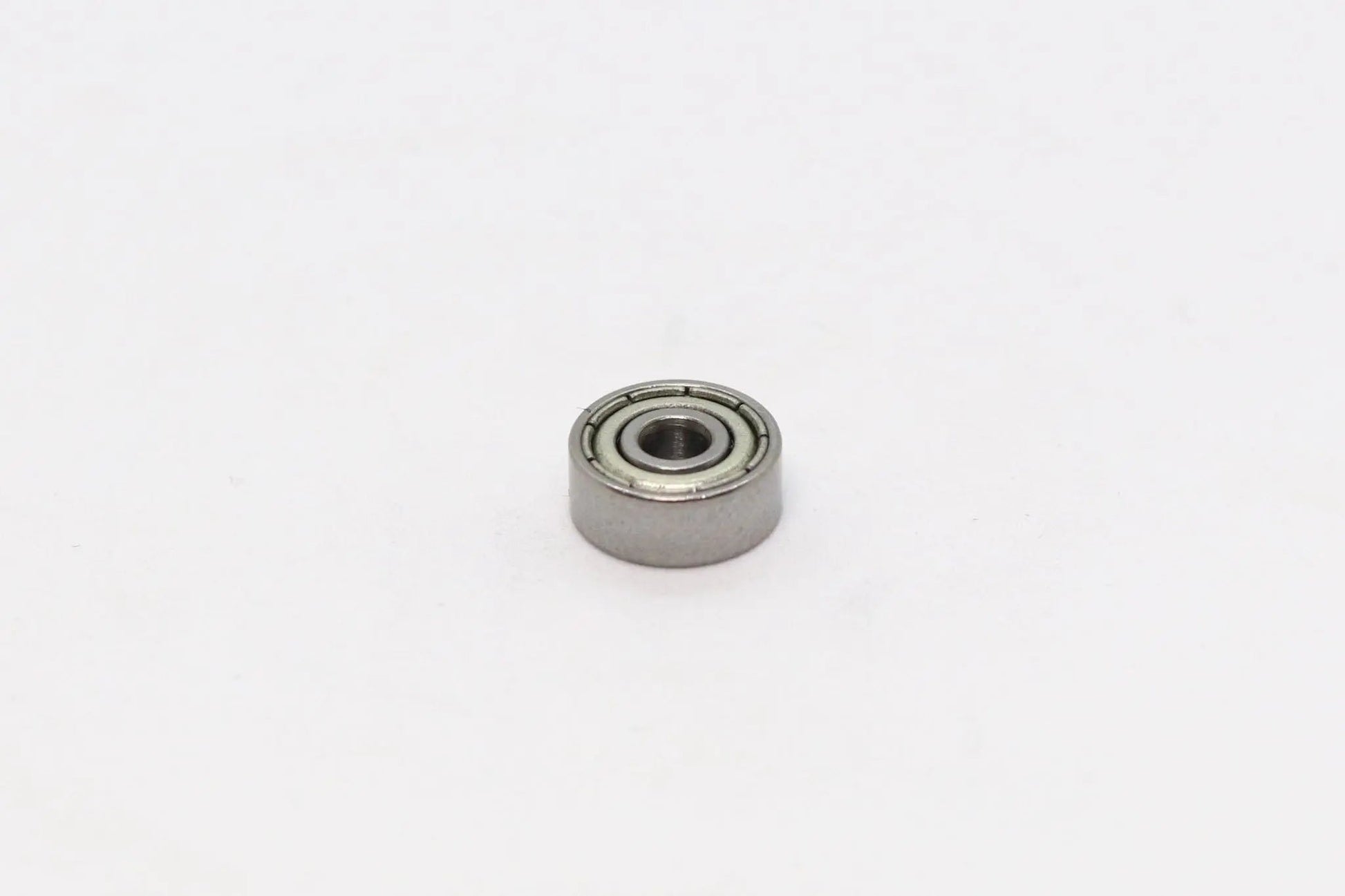 Un petit roulement à billes métallique vu de dessus sur fond blanc