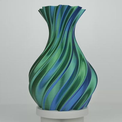 Vase imprimé en spirale bleu et vert sur un support blanc, centré sur fond gris
