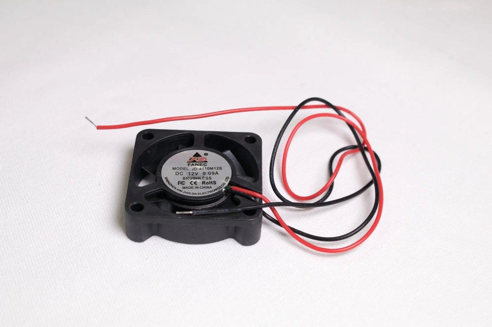 Petit ventilateur noir carré avec deux fils rouge et noir, posé sur fond blanc