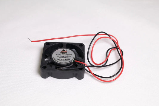 Petit ventilateur noir carré avec deux fils rouge et noir, posé sur fond blanc