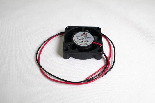 Petit ventilateur carré noir avec deux fils rouge et noir enroulés sur fond blanc