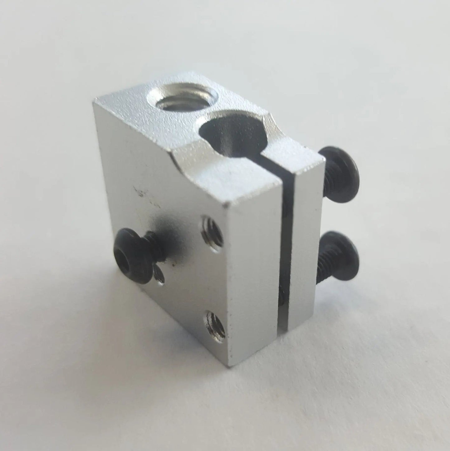 Bloc chauffant en aluminium argenté, vu en biais sur fond blanc, avec vis noires et trous filetés visibles