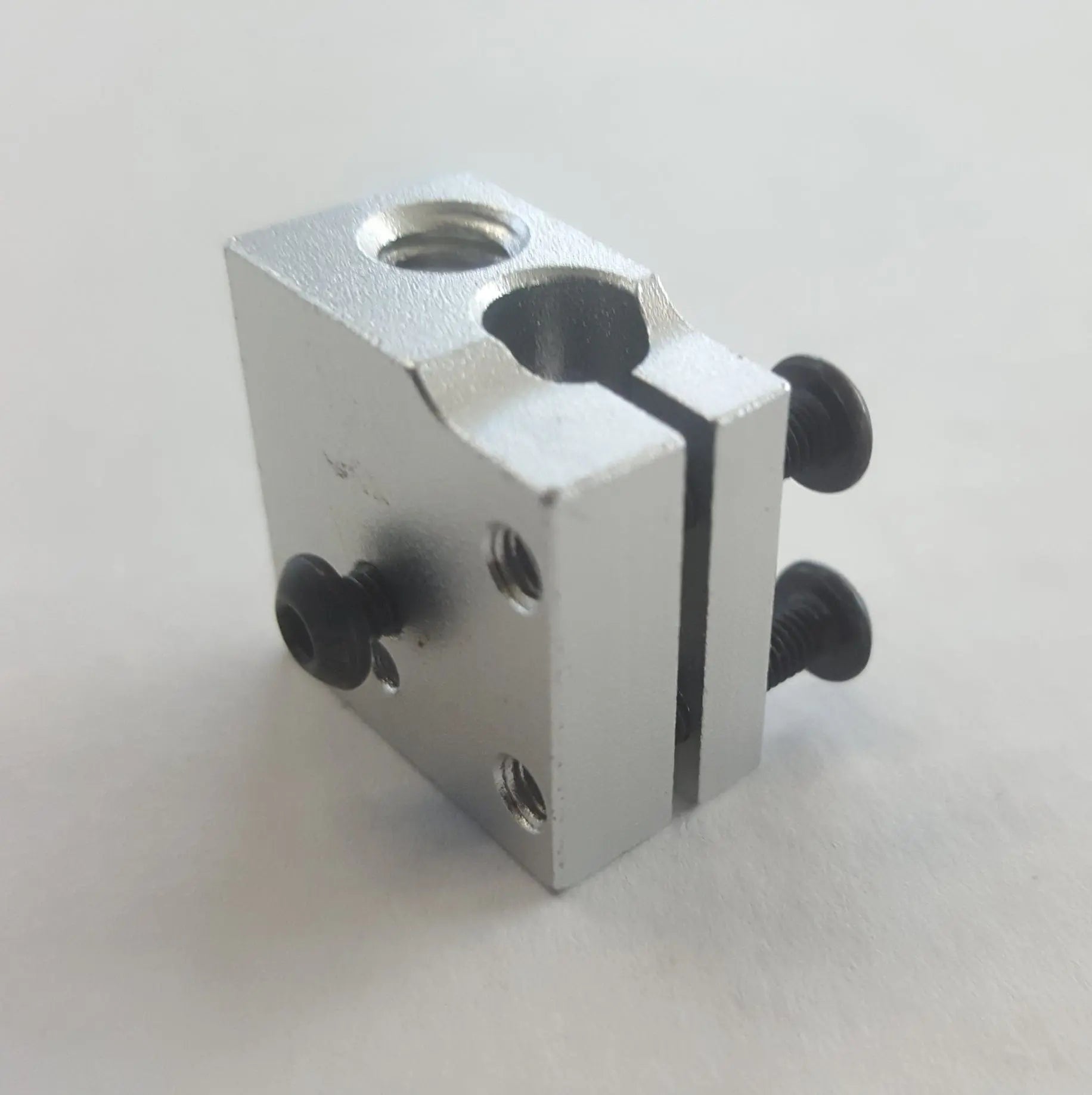 Bloc chauffant en aluminium argenté, vu en biais sur fond blanc, avec vis noires et trous filetés visibles