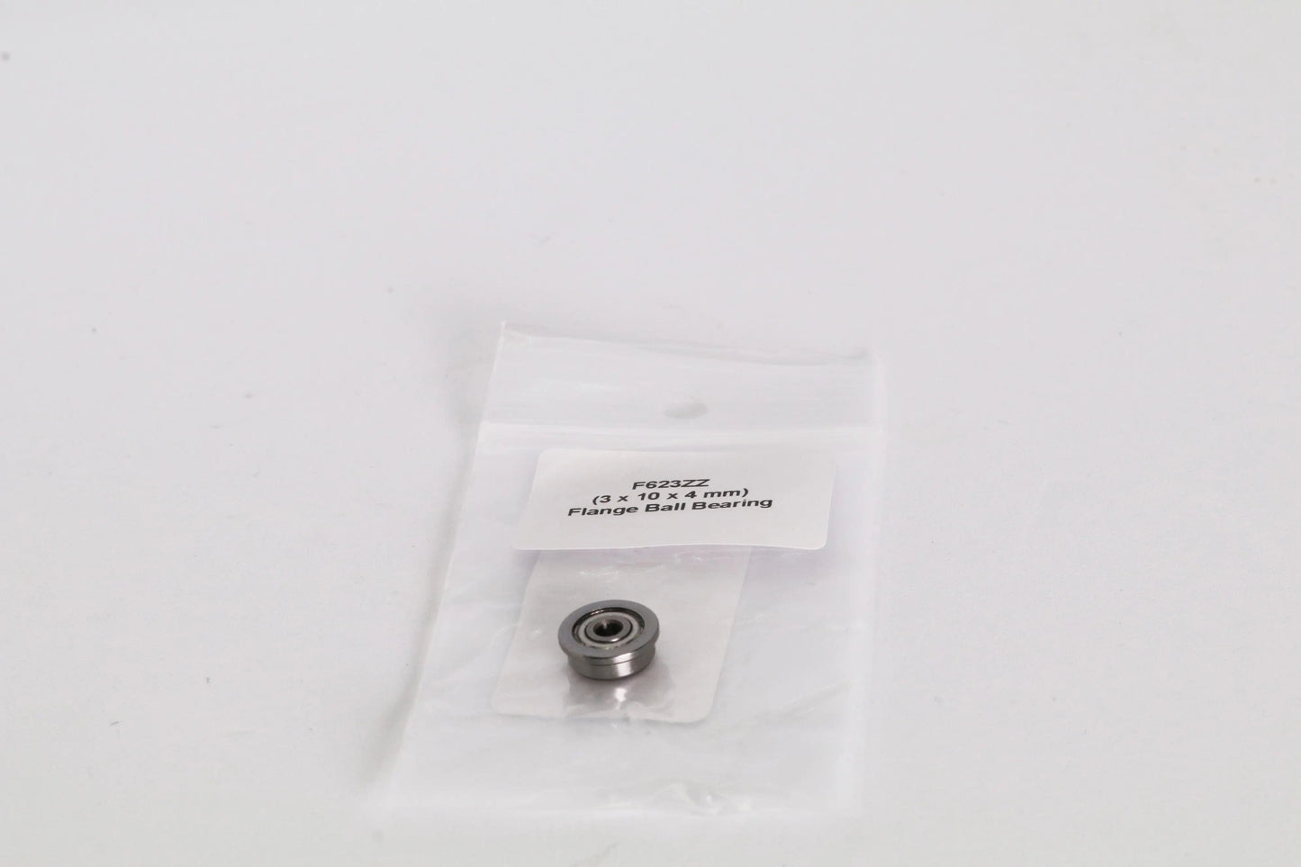 Petit roulement à billes à bride dans un sachet plastique transparent avec étiquette, posé sur fond blanc