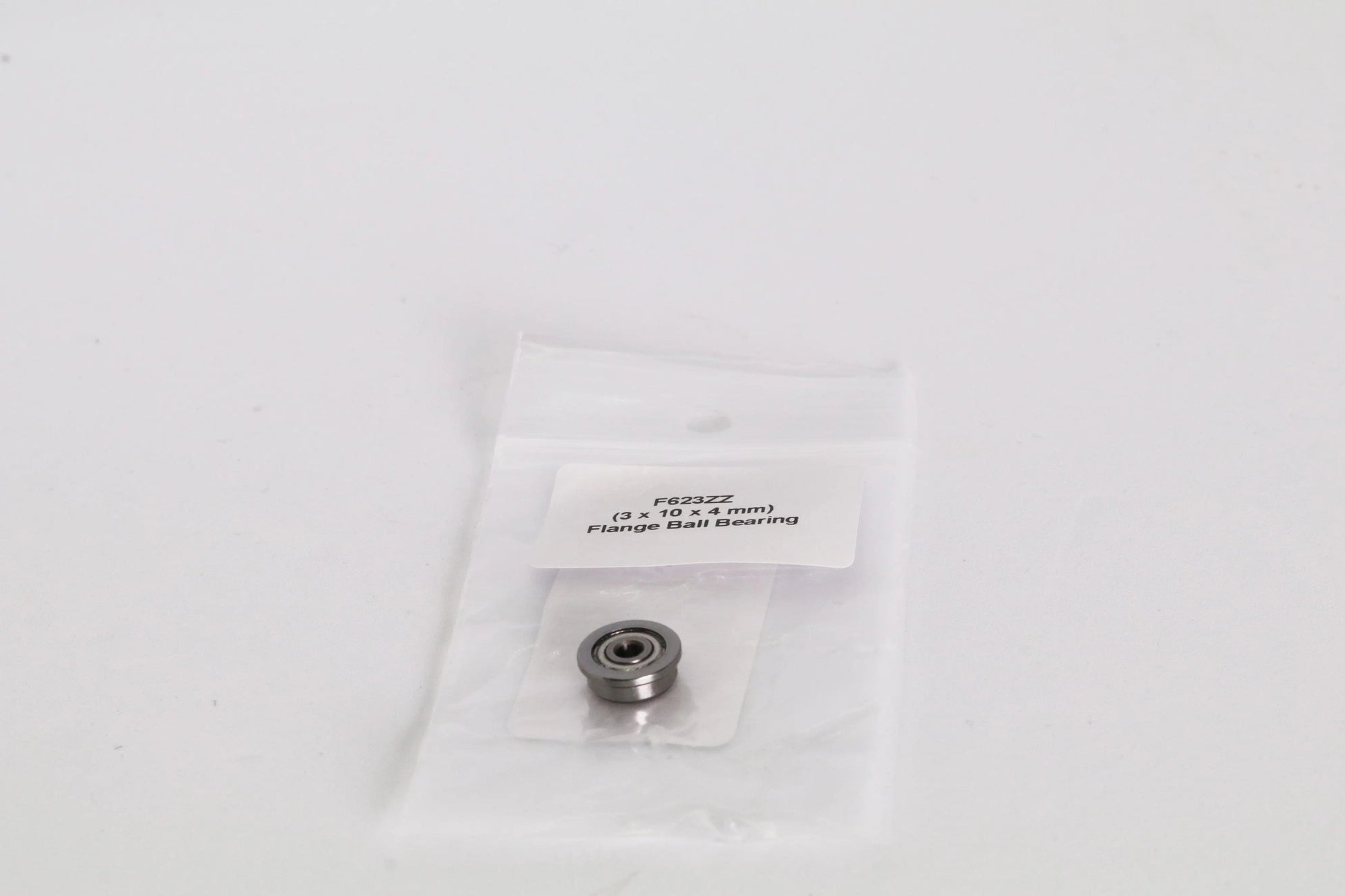 Petit roulement à billes à bride dans un sachet plastique transparent avec étiquette, posé sur fond blanc
