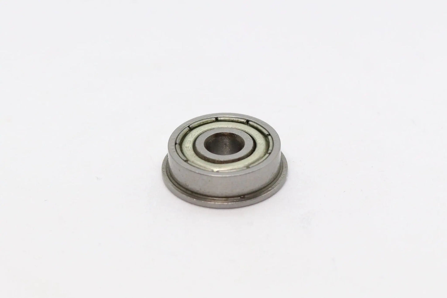 Vue rapprochée d’un petit roulement à billes à bride métallique sur fond blanc