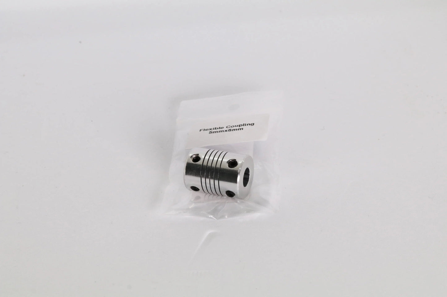 Petit accouplement flexible métallique dans un sachet plastique, vu de face sur fond blanc