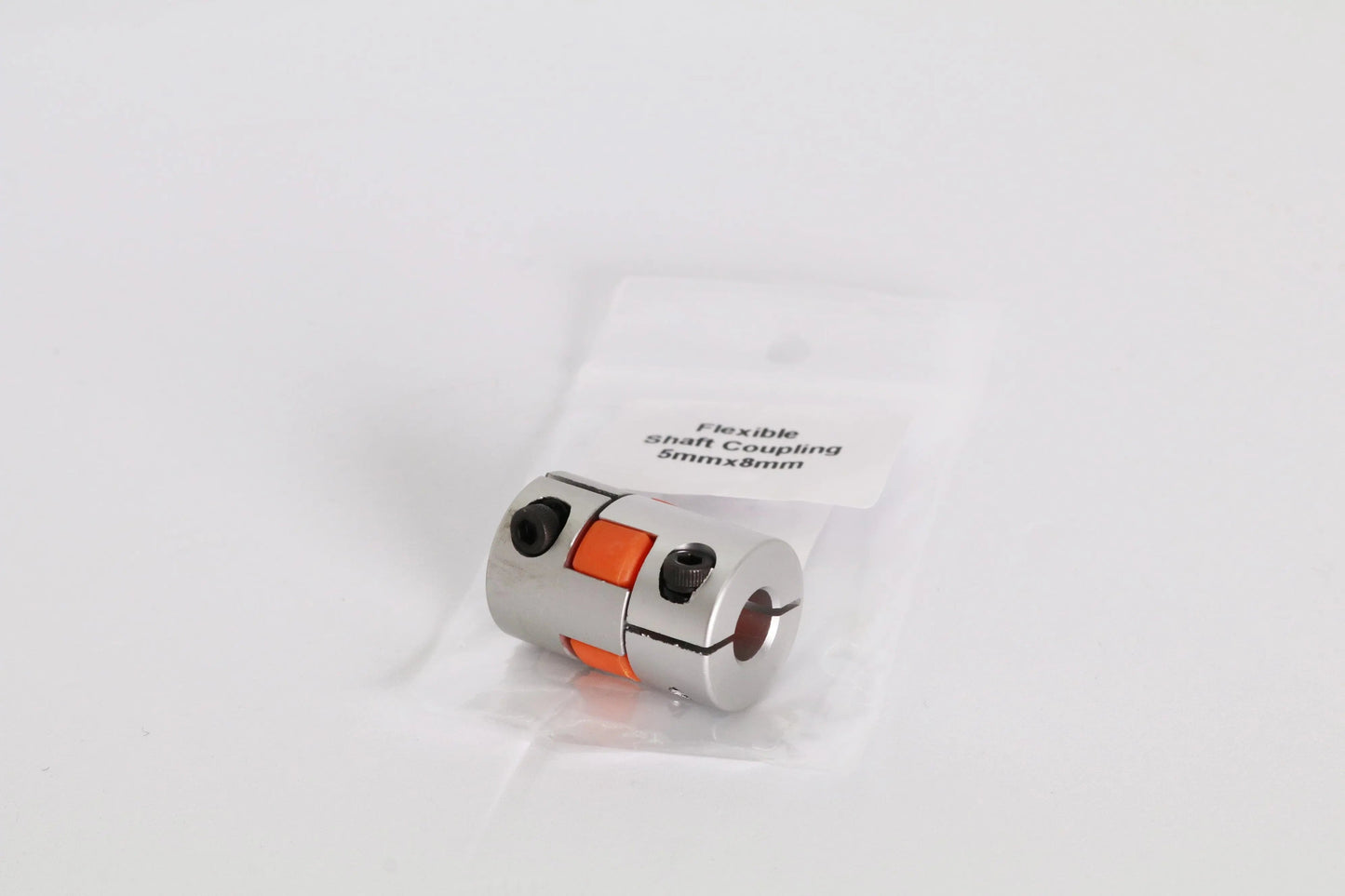 Petit coupleur d’arbre flexible en métal argenté avec insert orange, posé sur un sachet plastique
