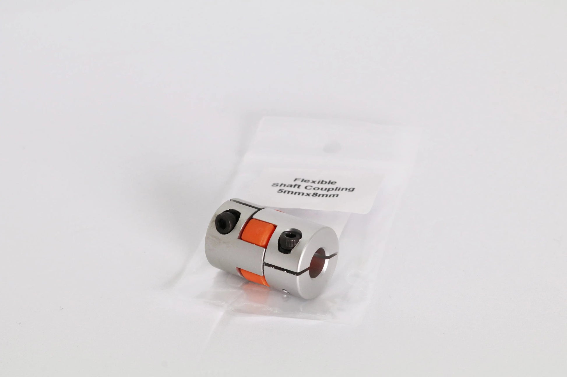 Petit coupleur d’arbre flexible en métal argenté avec insert orange, posé sur un sachet plastique