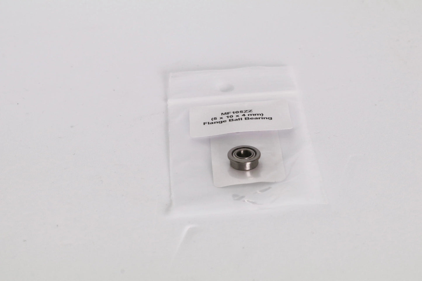 Petit roulement à bride en sachet plastique transparent sur fond blanc, étiquette visible et pièce métallique au centre