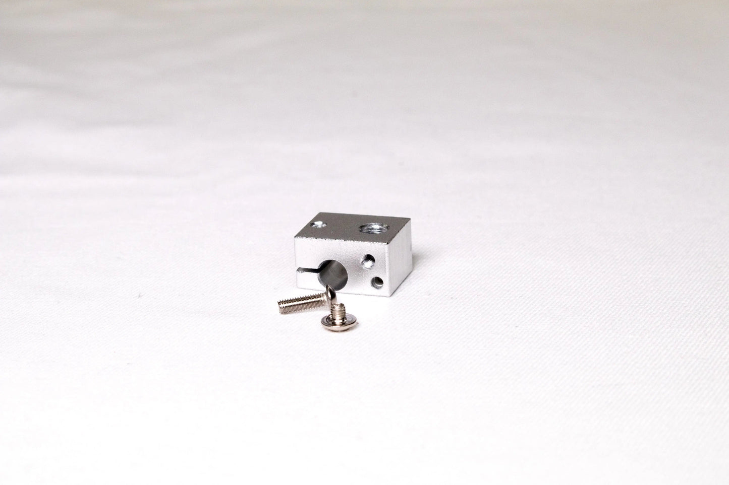 Petit bloc chauffant en aluminium argenté avec deux vis posés sur fond blanc