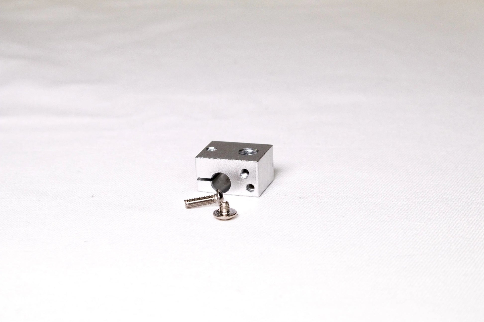 Petit bloc chauffant en aluminium argenté avec deux vis posés sur fond blanc